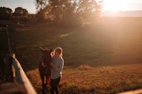 A caretaker gently leading a horse from the stable to the pasture on a sunny morning.