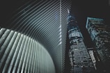 A futuristic architectural scene featuring the interior of a building with sleek, curved ribs and two adjacent skyscrapers with numerous lit windows against a night sky.