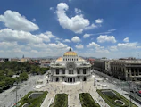 a large building with a gold domed roof surrounded by a parking lot with Palacio de Bellas Artes in the background