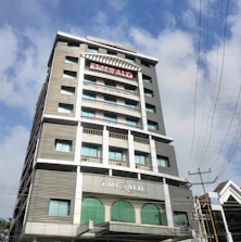 A tall multi-story building named Emerald Residency is shown with a modern architectural design, featuring large windows and a prominent sign at the top. The building is surrounded by a clear blue sky with some clouds and nearby power lines.