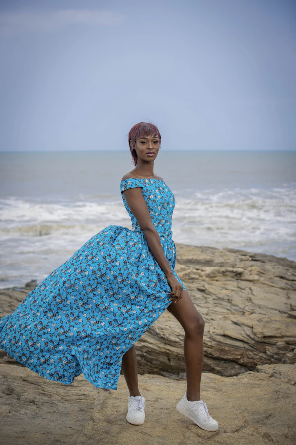 Model in a flowing blue Ankara maxi dress by the sea