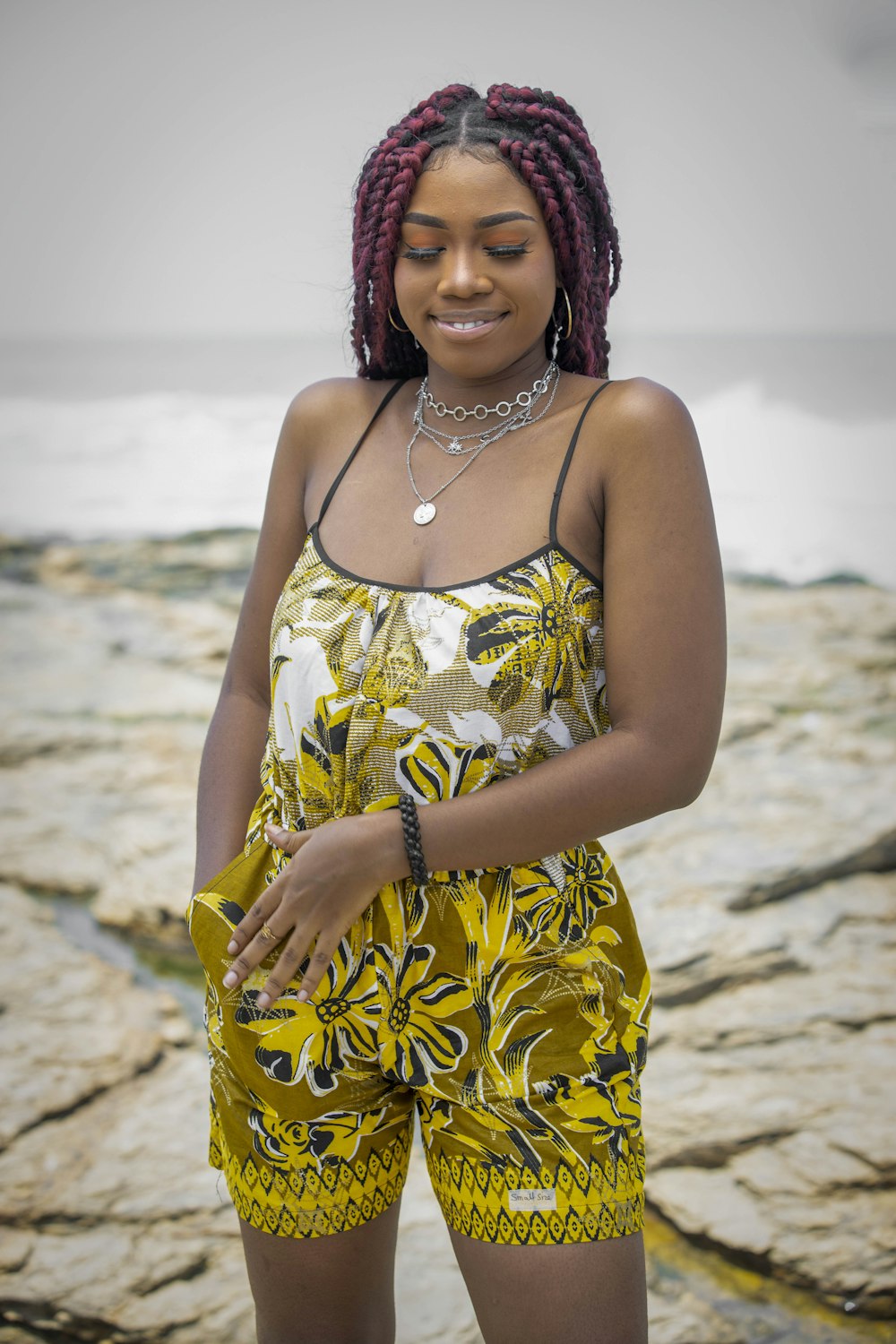 a woman in a yellow and black dress standing on a rocky beach