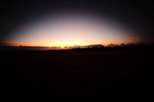 A serene landscape at twilight with dark silhouettes and a hint of violet in the sky.