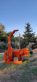 A sturdy German-made shredder working on a pile of green waste under a bright sky.