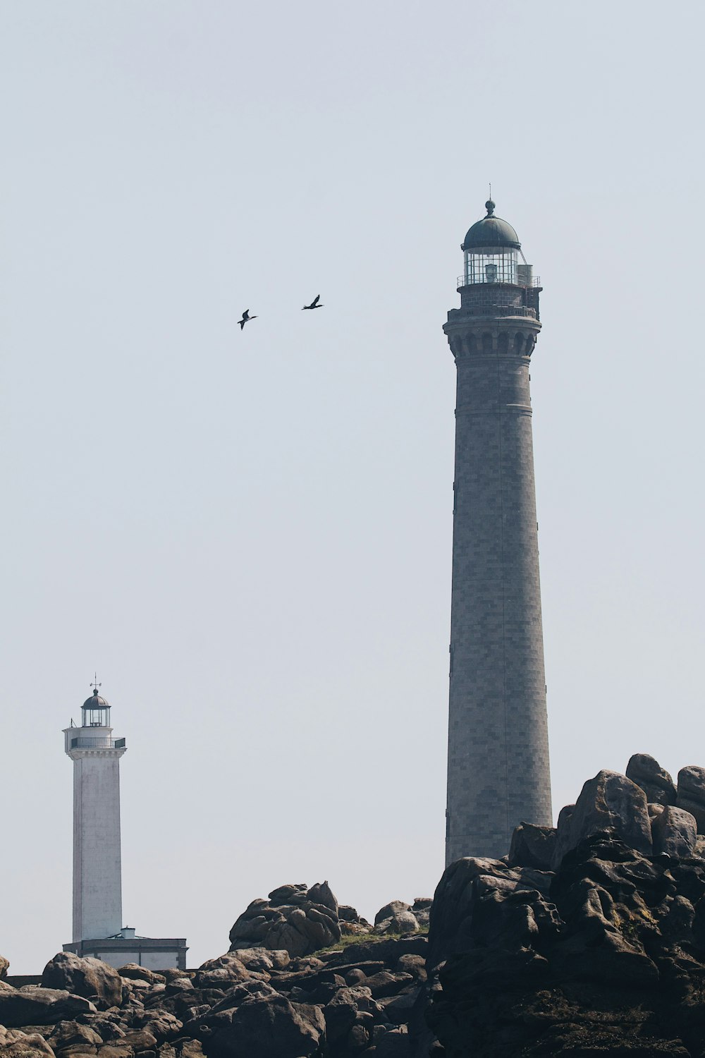 a couple of lighthouses on a rocky hill with birds flying around