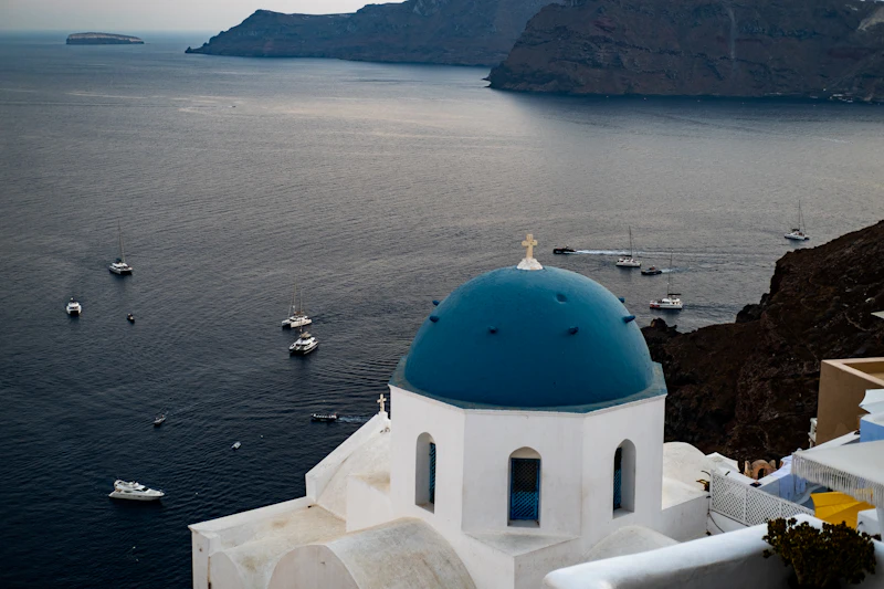 A blue-domed chapel above the caldera with boats on the water below