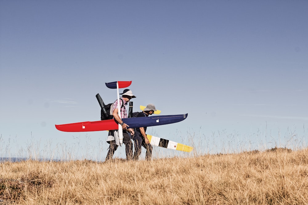 a couple of men carrying a surfboard in a field