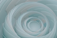 A series of smooth, layered, spiral patterns creating a tunnel-like effect. The shapes are delicate and organic, with a fluid, continuous form that draws the eye inward.