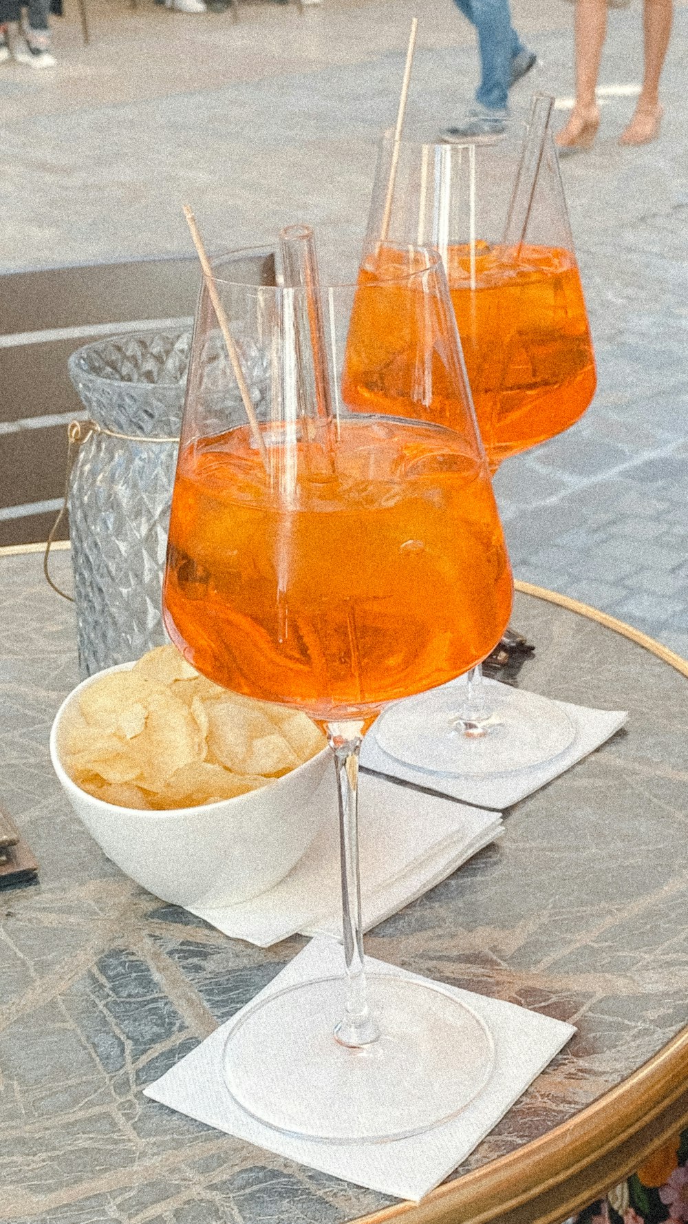 a glass of orange drink with a straw and a bowl of potato chips