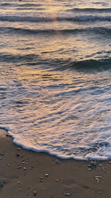 Gentle waves washing over smooth beach pebbles at sunset with warm colors.
