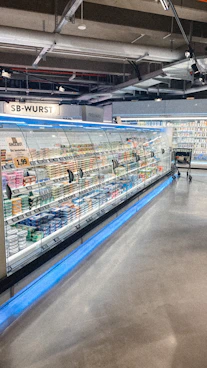A busy supermarket aisle filled with modern refrigeration and shelving units.