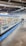 A supermarket aisle contains a long refrigerated display filled with various packaged products. Bright lighting illuminates the area, highlighting items such as meats and dairy. The floor is polished concrete, and a shopping cart is visible in the distance.