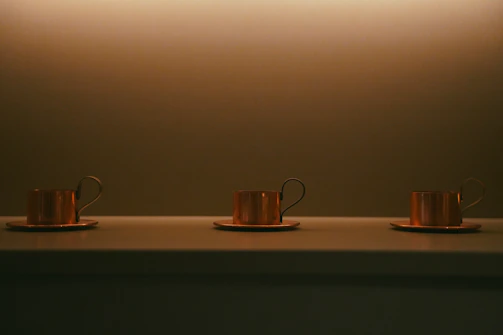 A set of copper tumblers arranged on a rustic wooden table, catching warm sunlight.