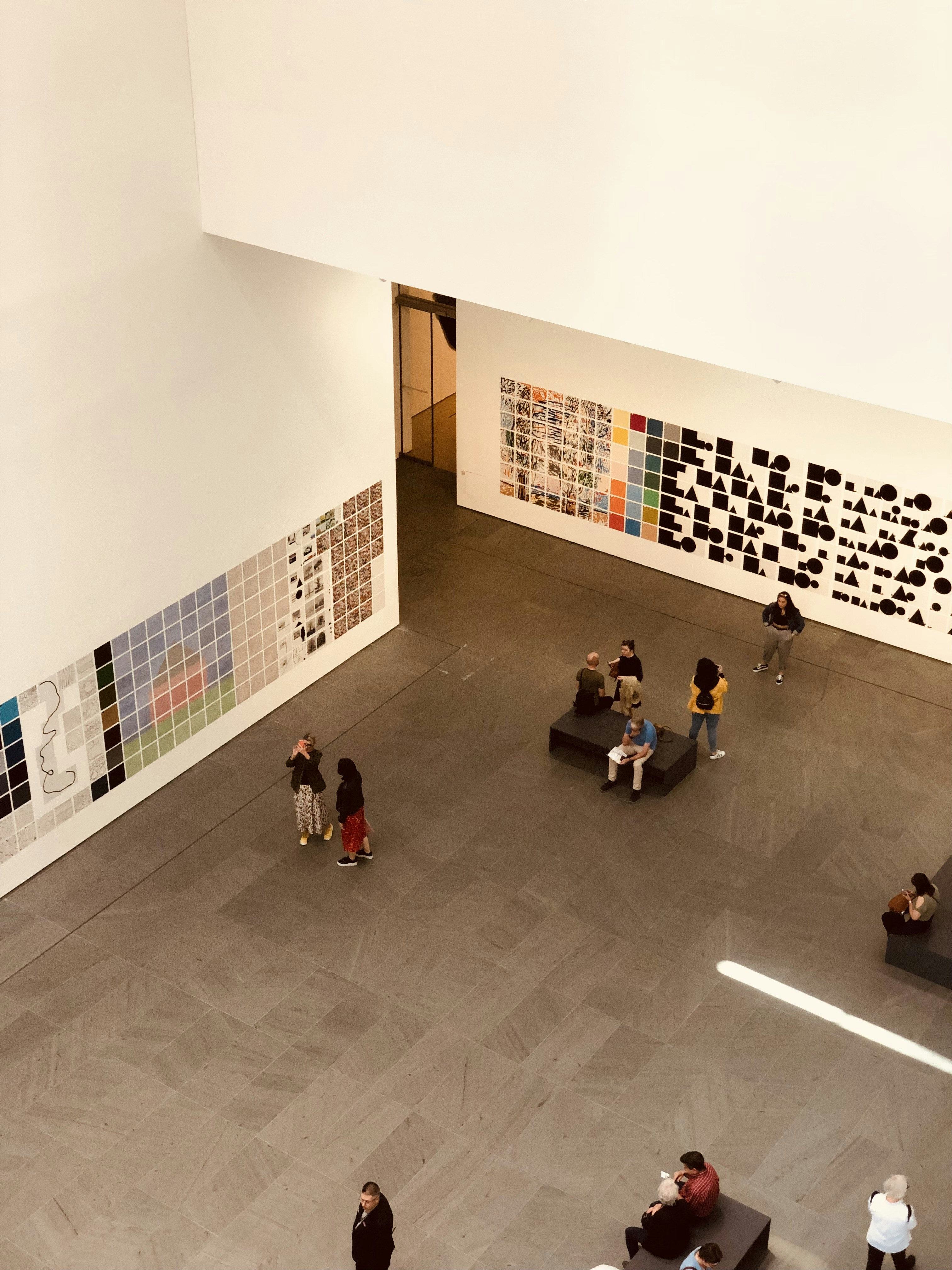 Sala de exposición de arte contemporáneo con paredes blancas, instalación de luz de neón y visitantes observando las obras