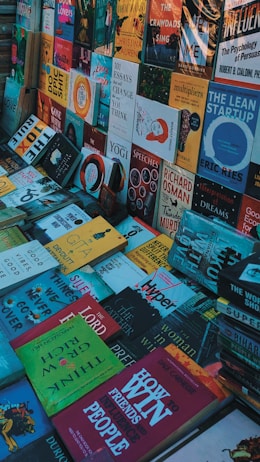 A variety of books are arranged in a cluttered, overlapping manner, showcasing a multitude of titles and colorful covers. The books are laid out horizontally and vertically, with genres ranging from self-help and fiction to non-fiction and essays.