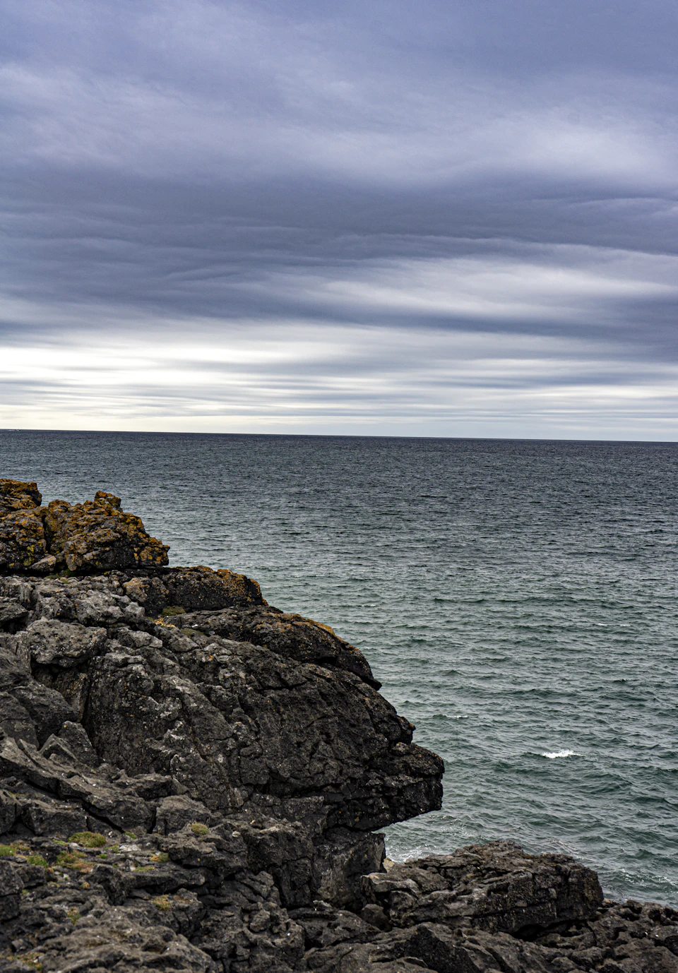 Rocky cliff overlooking the ocean with cloudy sky above in rugged natural landscape setting
