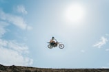 A rider launching off a dirt ramp on a motocross bike under a bright sky.