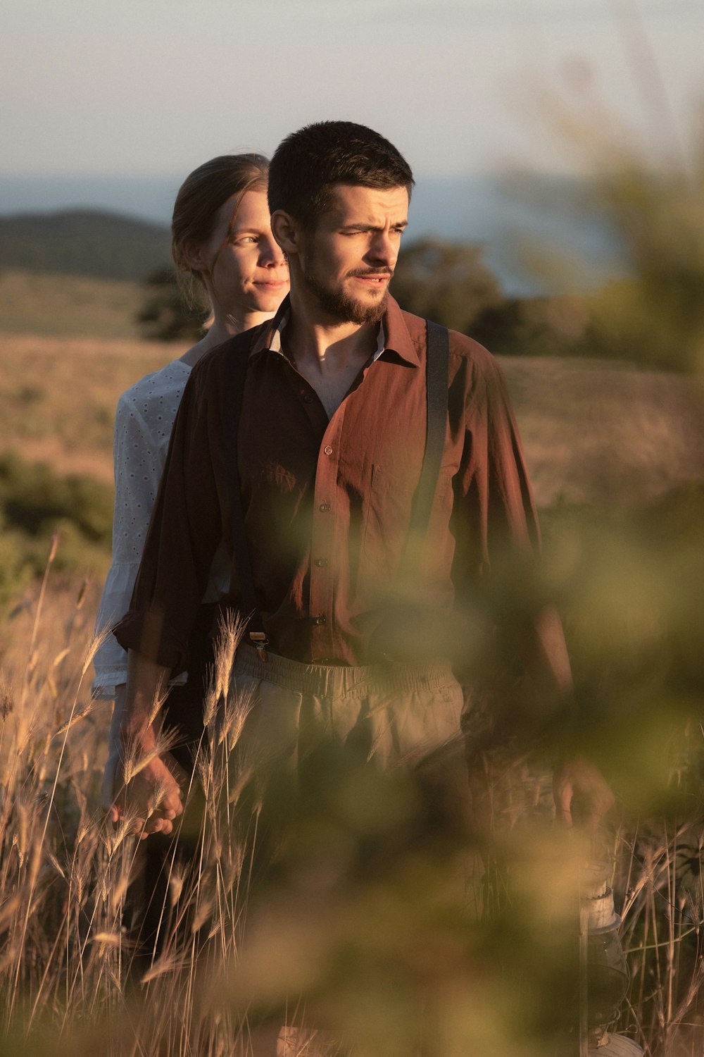 a man and woman standing in a field of tall grass