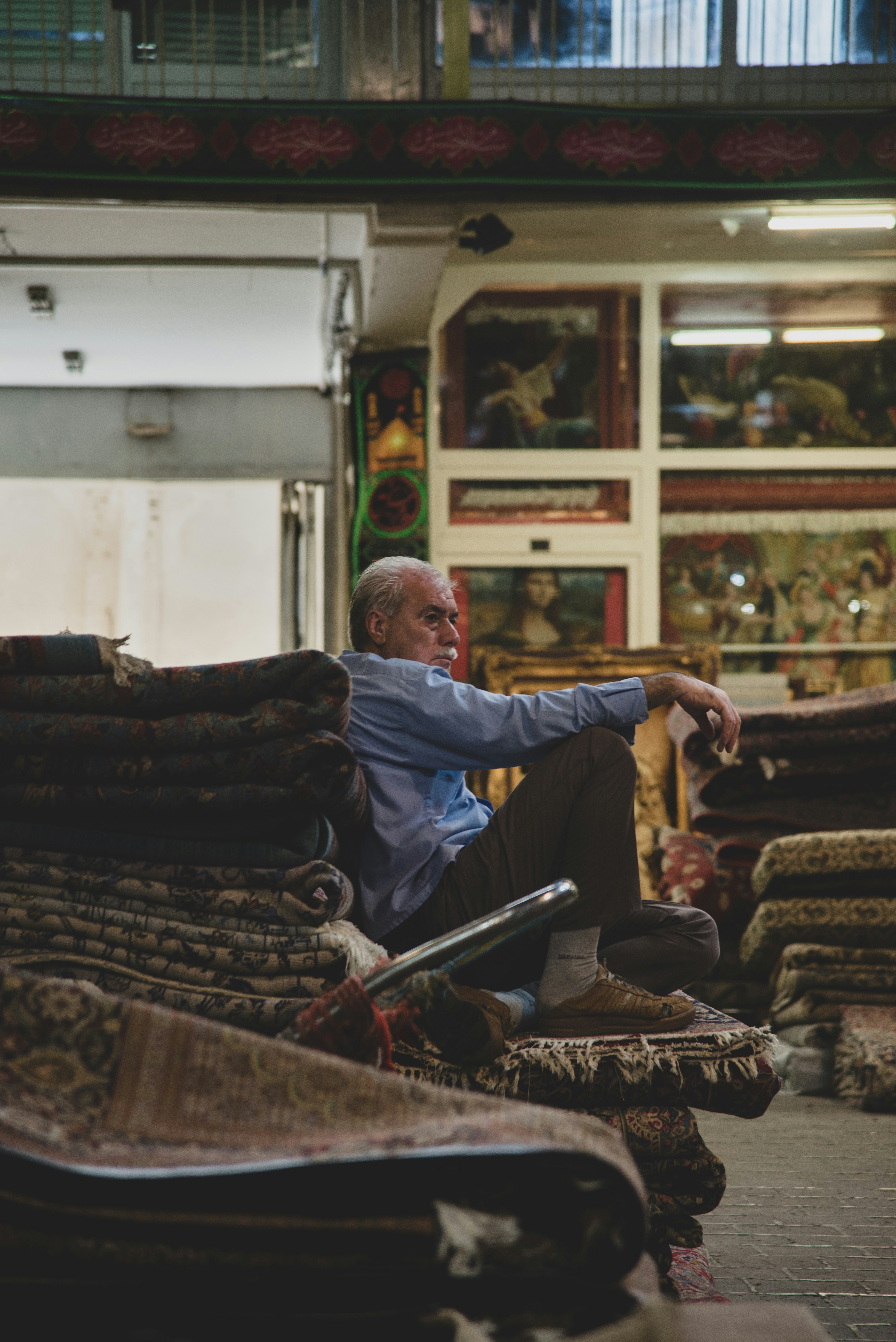 Hombre mayor sentado entre alfombras apiladas en una tienda