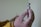 A gloved hand holds a vial of Pfizer-BioNTech vaccine with a blurred background, creating a clinical and focused scene.