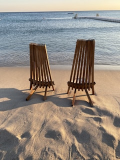 Wooden deck chairs facing the sparkling sea under a clear blue sky at sunset.