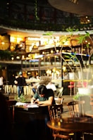 A detective taking notes while watching a subject in a café setting