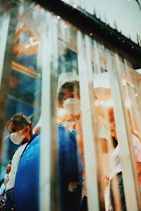 Children wearing face masks are visible behind a glass partition with droplets. One child appears to be holding up a peace sign, adding a sense of playfulness. The ambient lighting creates a soft, warm atmosphere.