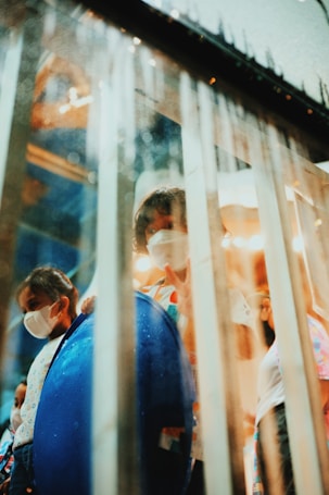 Children wearing face masks are visible behind a glass partition with droplets. One child appears to be holding up a peace sign, adding a sense of playfulness. The ambient lighting creates a soft, warm atmosphere.