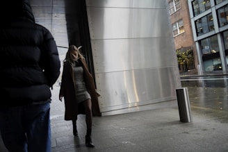 A model wearing layered street style clothes walking in an urban setting.