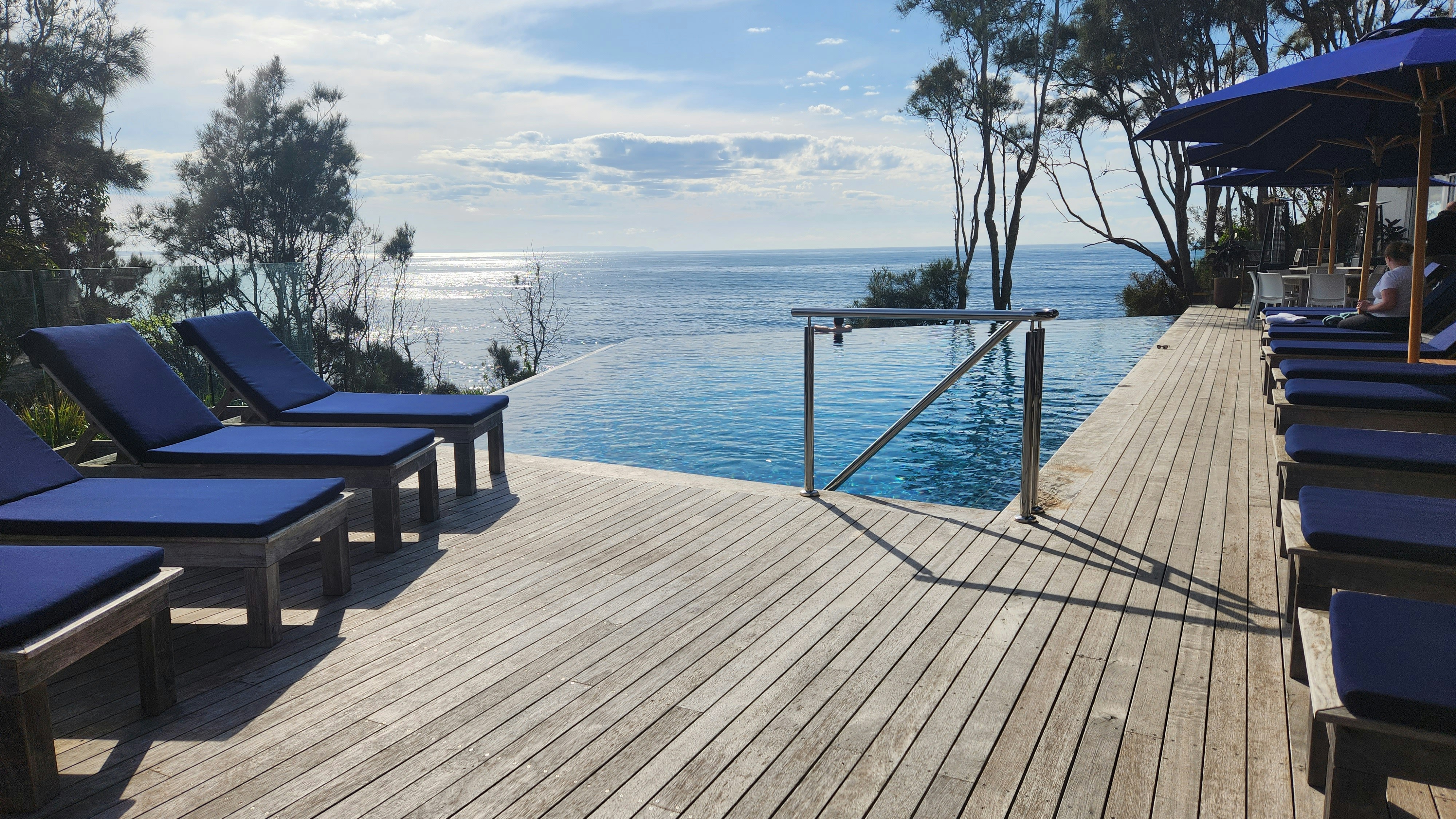 Infinity pool with lounge chairs, landscaped garden, clear blue sky, luxury outdoor living