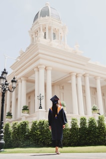 a man in a graduation cap and gown standing in front of a white building