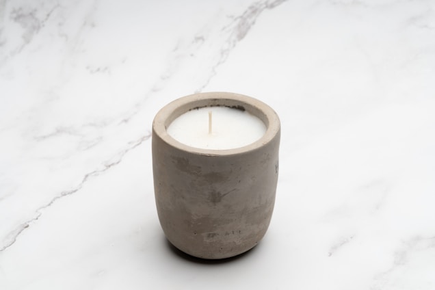 Hand pouring candle wax into a handcrafted concrete pot surrounded by natural elements.