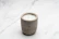 A minimalist ceramic candle holder with a softly glowing candle casting warm shadows on a clay-textured table.