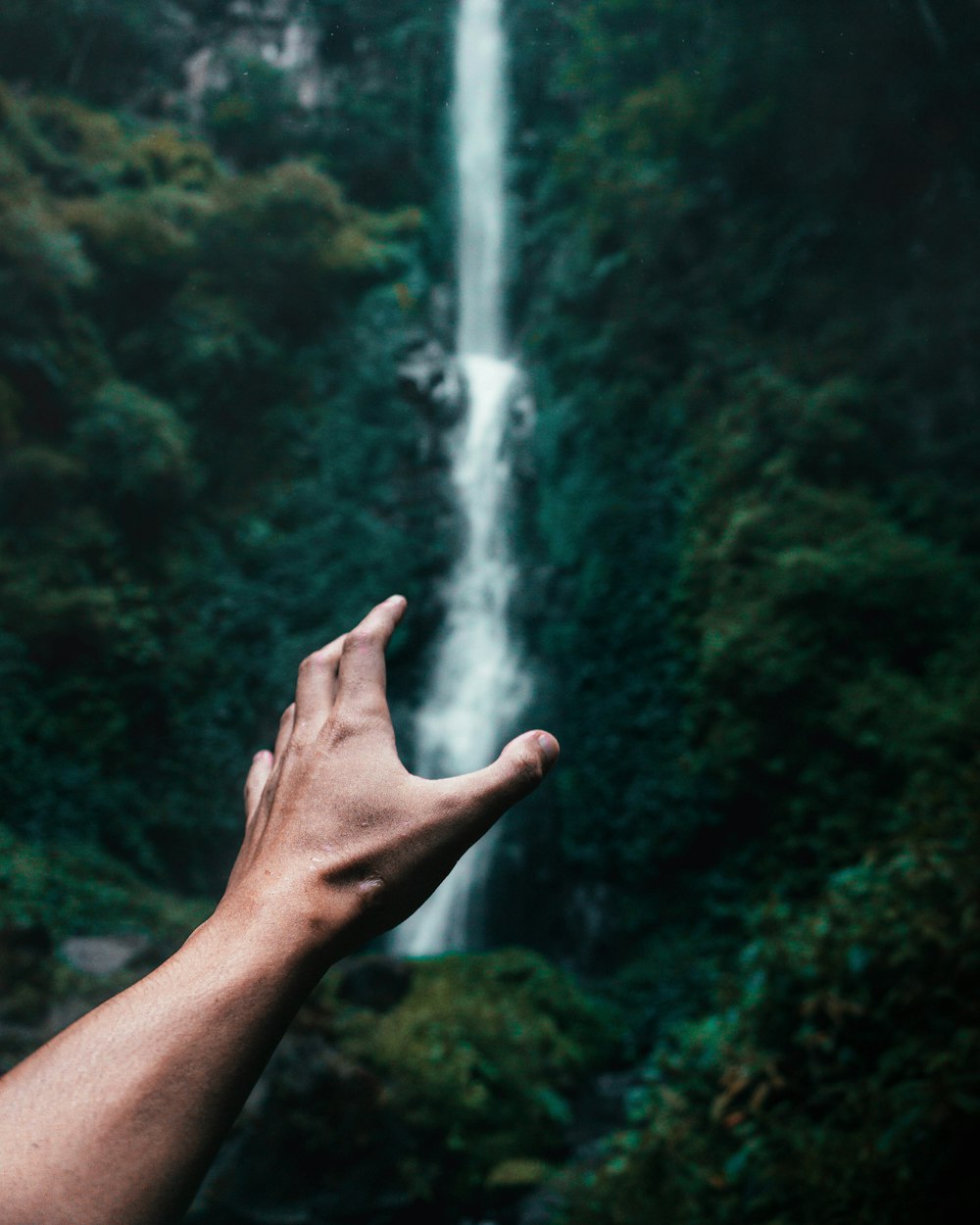 a hand reaching out to a waterfall