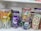 A shelf displays a variety of colorful candies in transparent plastic jars. On the left, there are lollipops with orange and yellow colors. The center jar contains Cadbury Dairy Milk chocolates, noticeable by the distinctive purple packaging. Another jar holds candies shaped like butterflies in pastel shades. On the right, wafer cones with pink and green colors are visible.
