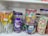 A shelf displays a variety of colorful candies in transparent plastic jars. On the left, there are lollipops with orange and yellow colors. The center jar contains Cadbury Dairy Milk chocolates, noticeable by the distinctive purple packaging. Another jar holds candies shaped like butterflies in pastel shades. On the right, wafer cones with pink and green colors are visible.