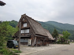 a wood building with a car parked in front of it with Shirakawa in the background
