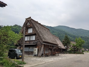 a wood building with a car parked in front of it with Shirakawa in the background