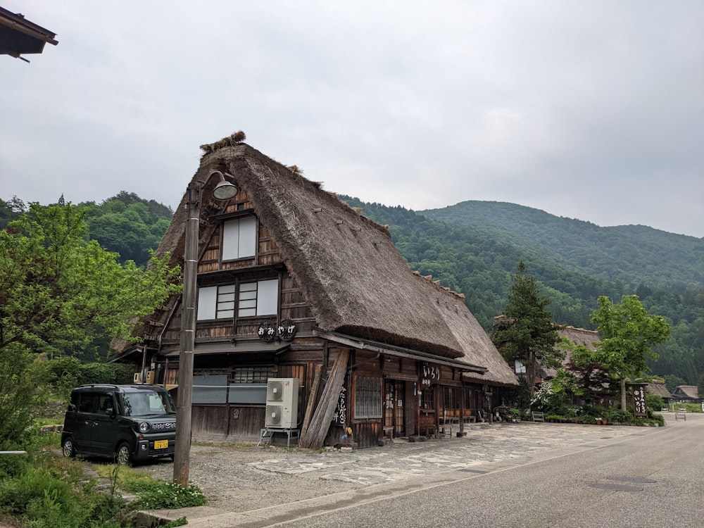 un edificio de madera con un coche aparcado delante de él con Shirakawa al fondo