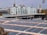 A large array of solar panels is installed on the roof of a stadium building. Behind the stadium, there are several buildings, one of which is labeled 'Brabourne Stadium'. The sky is overcast, and there are trees visible in the foreground.
