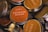Several round, metal tins with lids featuring labels that have various aromatic scents such as Denmark Hygge and Sicily. The labels are mostly orange and beige with a mix of English and non-English languages detailing the scents.