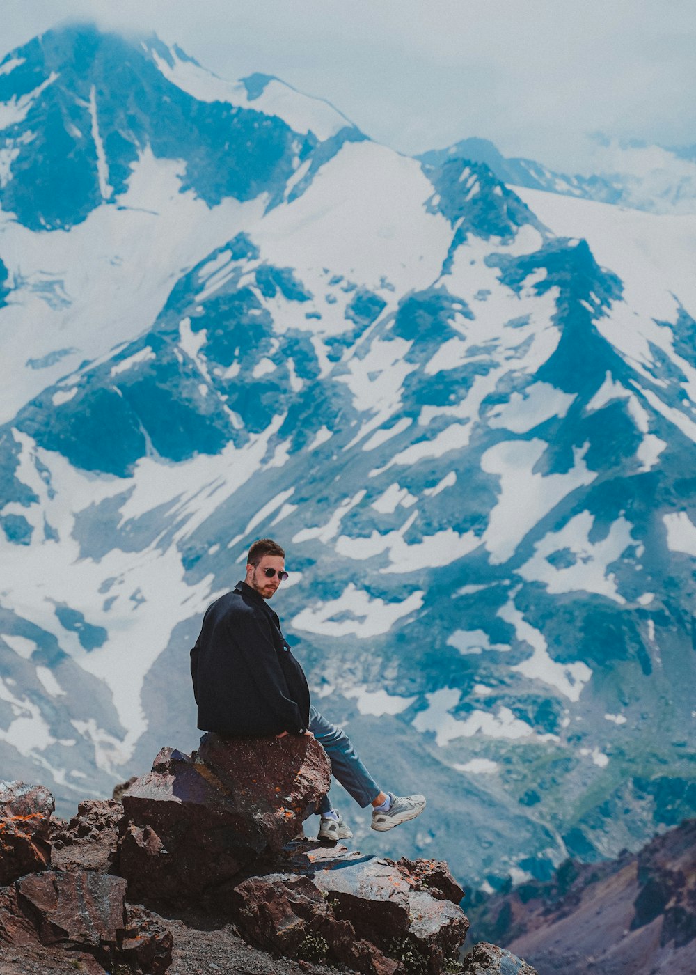 a man sitting on a rock with a mountain in the background