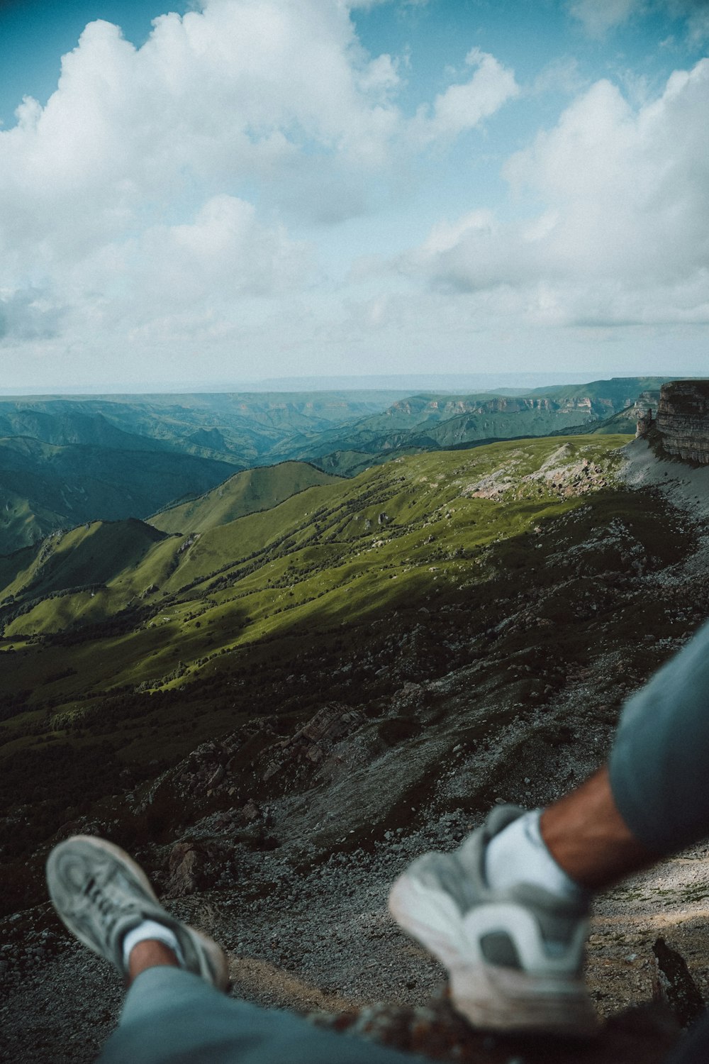 a person's legs on a rock ledge overlooking a valley