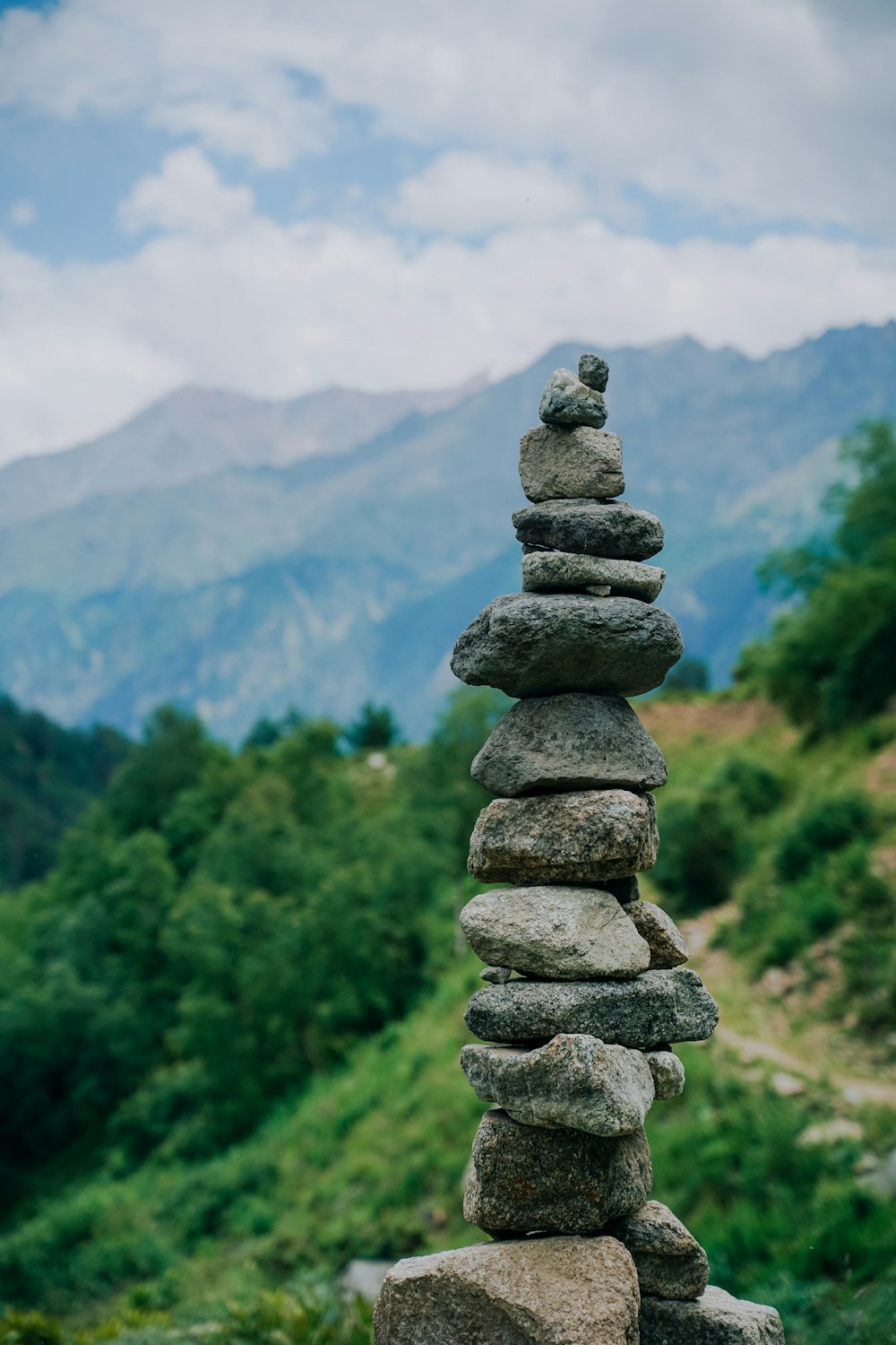 a stack of rocks with trees and mountains in the background