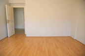 Empty interior space featuring natural light on wooden flooring and white walls.