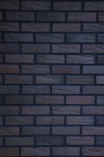 A pattern of uniformly arranged dark brown and black bricks, featuring a consistent size and layout. The surface texture of the bricks appears slightly rough and weathered.