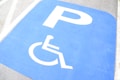 A blue parking space reserved for disabled access, marked with a white wheelchair symbol and a large 'P'. The background includes gray pavement and white lines.