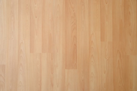 Smooth, light wooden surface with subtle grain patterns. The texture appears polished and seamless, suggesting laminate or hardwood flooring.