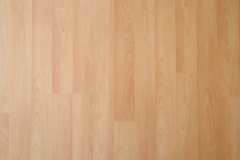 Smooth, light wooden surface with subtle grain patterns. The texture appears polished and seamless, suggesting laminate or hardwood flooring.