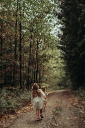 a couple of children walking on a path in the woods